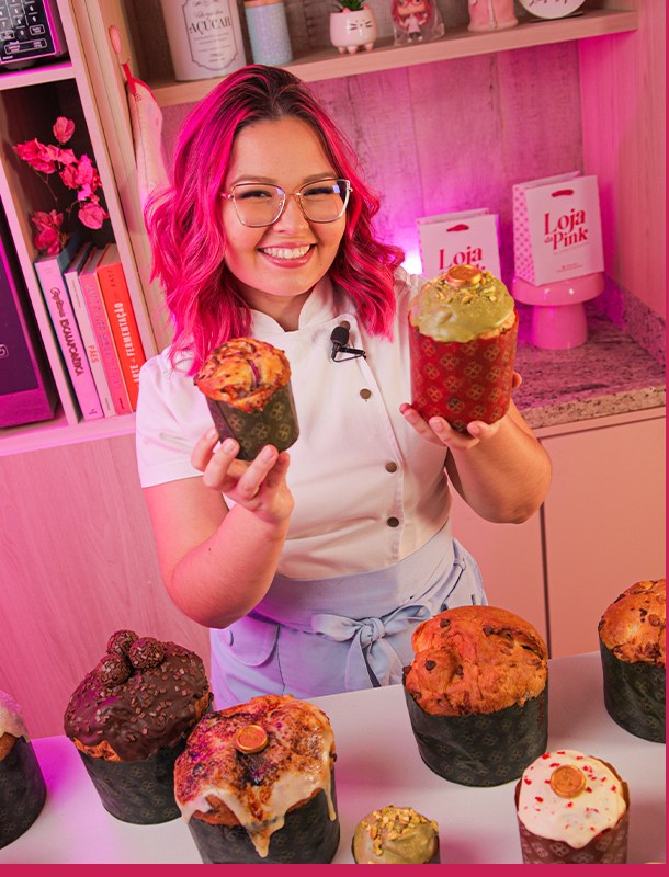 Chef Laís Lopes segurando dois panetones decorados na cozinha rosa